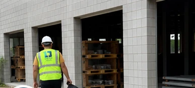 Crew member in hard hat and vest hauling a debris bag out of a cinder-block building under construction