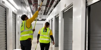 Crew members sweeping and dusting a self-storage hallway lined with roll-up doors